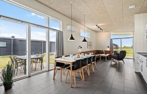 Una cocina amplia con ventanas grandes, un comedor con una mesa larga y un rincón de descanso acogedor con un sofá y sillones.