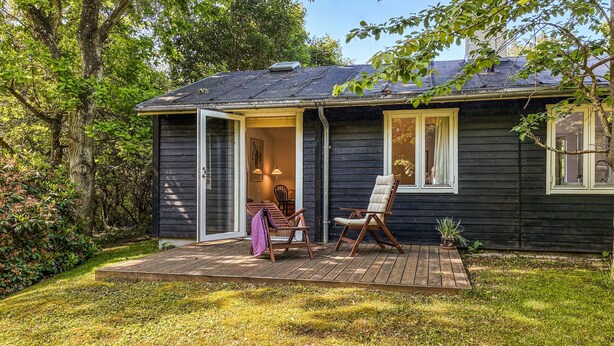 Een houten huis met een veranda, twee stoelen en een tafel.