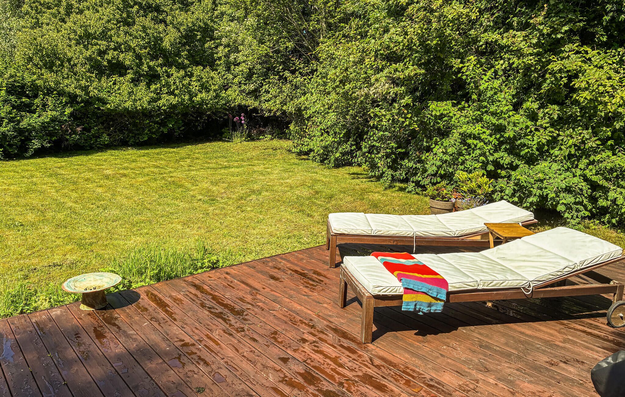 Eine Holzterrasse mit zwei Liegestühlen, einer mit einer bunten Decke.