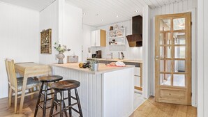 A kitchen with a central island, wooden chairs, a dining table, and a wooden door with glass panels. - 4 bedroom nice home in Glesborg (Glesborg)