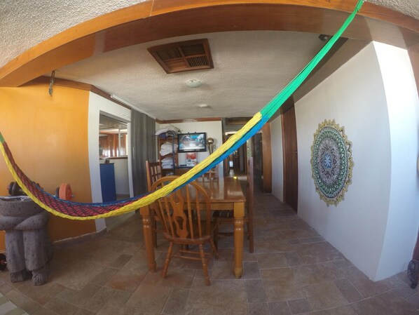 A dining area with a hammock, a statue, and a television in the background. - Izsla Hostel (Playa del Carmen)