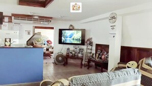 A hotel lobby with a reception desk, a television mounted on the wall, and a sofa in the seating area. - Izsla Hostel (Playa del Carmen)
