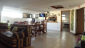 A living room with a sofa, dining table, chairs, and a TV. - Izsla Hostel (Playa del Carmen)