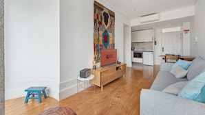A modern living room with a grey sofa, a wooden coffee table, and a colorful tapestry.