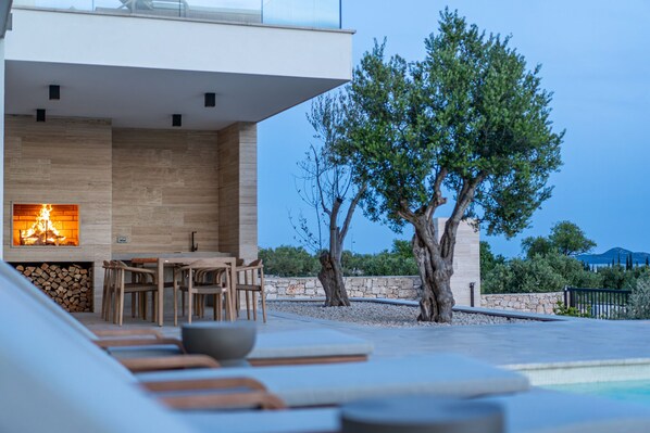 A modern outdoor seating area with a fire feature, stone walls, and a view of the landscape.