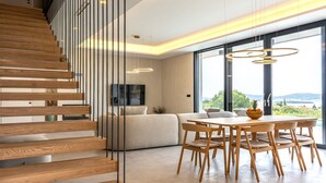 Un interior moderno con una escalera de madera, un comedor con sillas de madera y ventanas amplias que ofrecen vistas.