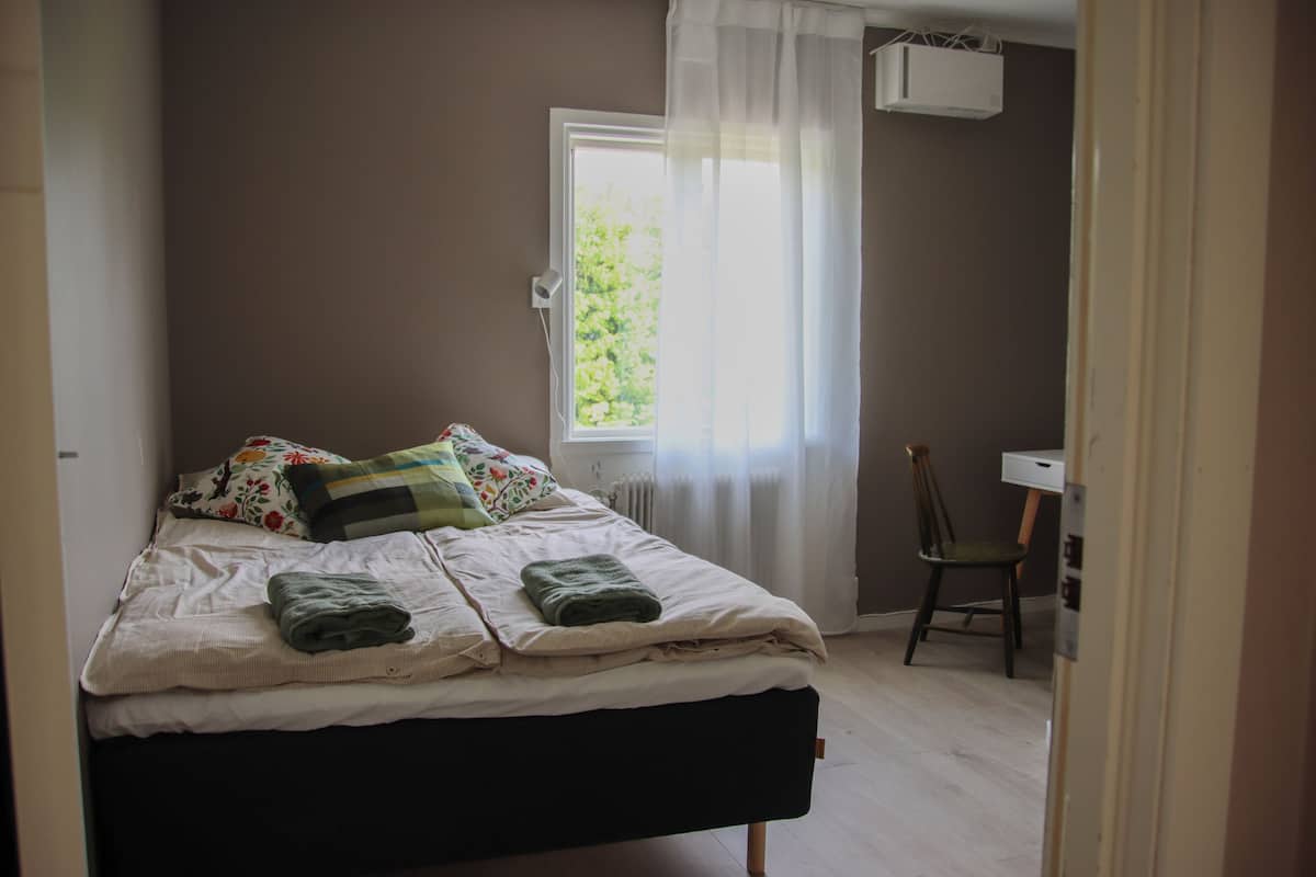 Ein Schlafzimmer mit einem Bett, einem Sessel, einem Fenster und einer Heizung.