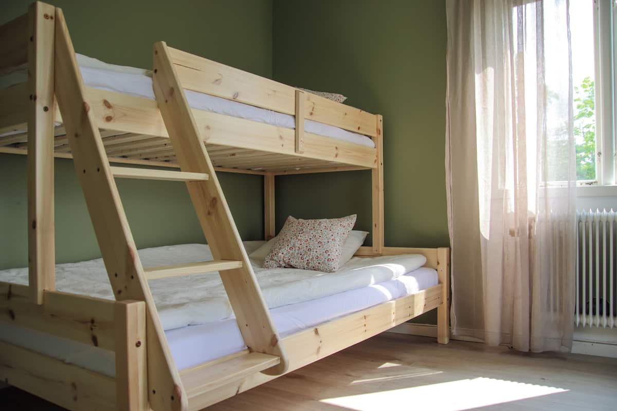 Ein Etagenbett mit einer Leiter, ein Fenster mit Vorhängen und eine Heizung.