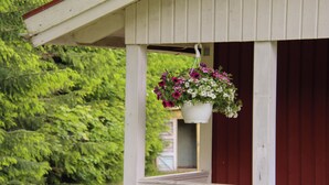 A white wooden structure with a hanging flower pot containing pink and white flowers. - Pintro B&B (Hagfors)