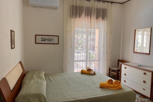 Une chambre à coucher avec un lit, une commode, une chaise et une fenêtre avec des rideaux.
