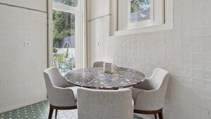 Una mesa redonda con cuatro sillas grises, un objeto decorativo pequeño sobre la mesa y vistas a zonas verdes a través de amplias ventanas.