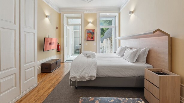 Un dormitorio bien iluminado con una cama grande, cabecera de madera, televisor de pantalla plana y vistas al exterior a través de un ventanal.