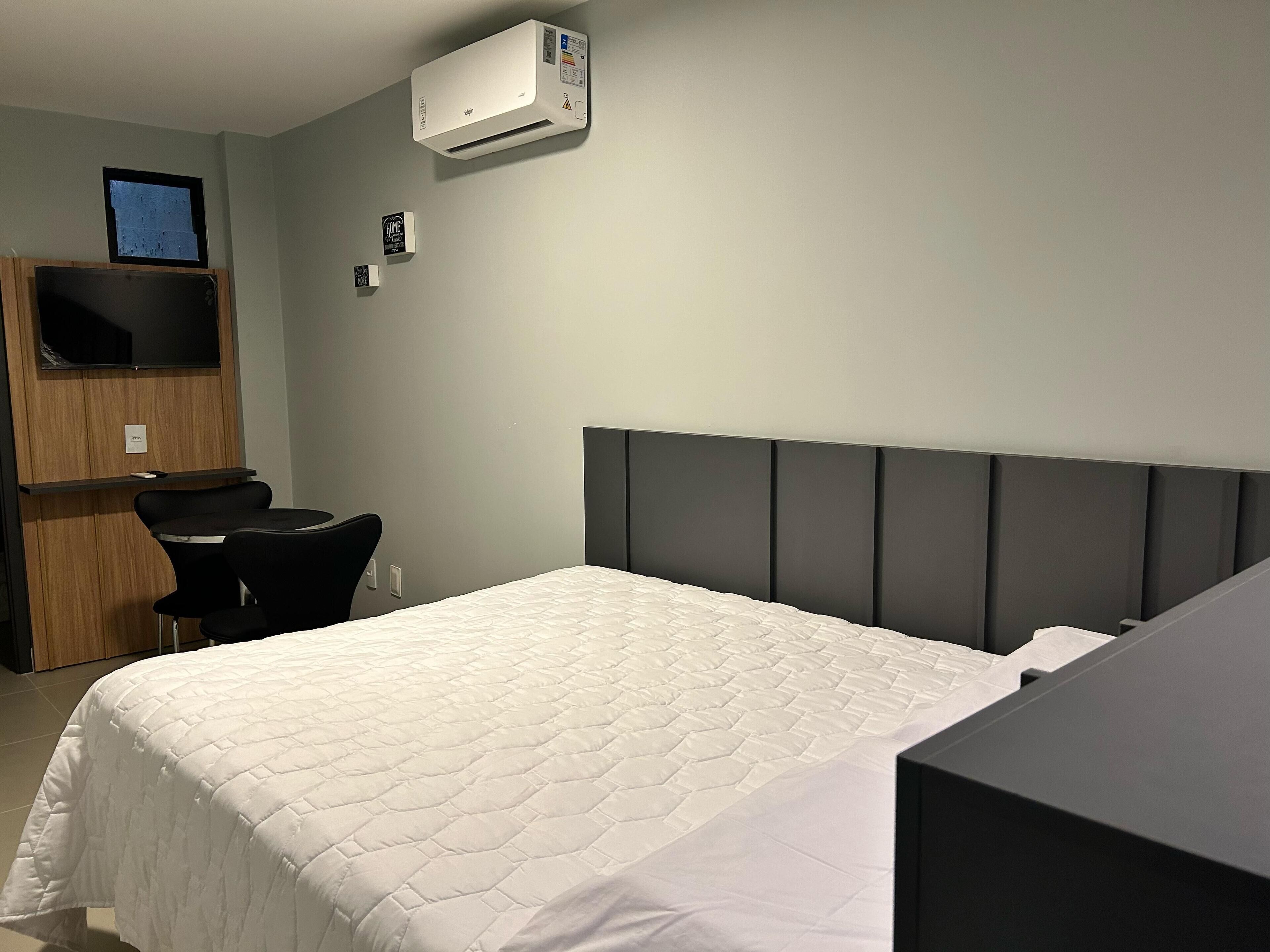 Habitació d'hotel amb llit, escriptori, cadira i aire condicionat.
