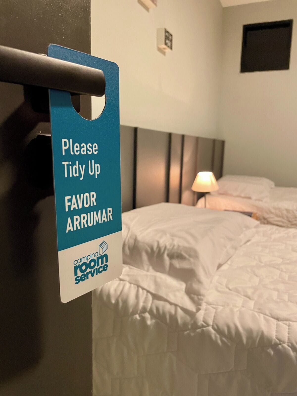 Une chambre d’hôtel avec un lit, une table de chevet, une lampe et un panneau invitant les clients à ranger la pièce.