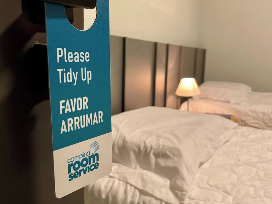 Ein Hotelzimmer mit Bett, Nachttisch, Lampe und einem Schild, das Gäste zur Reinigung auffordert.