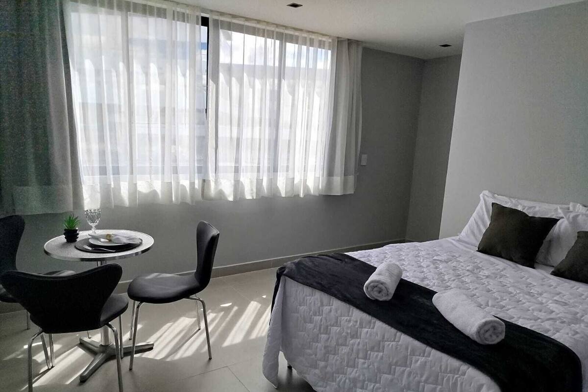 A hotel room with a bed, a small table with a glass, and two chairs.
