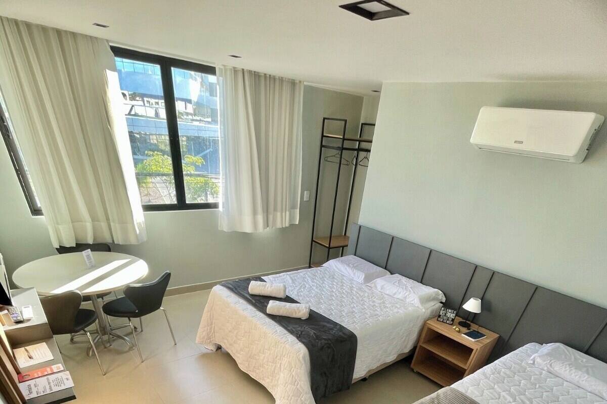 A hotel room with two beds, a desk, a chair, a small table, and a window with curtains.