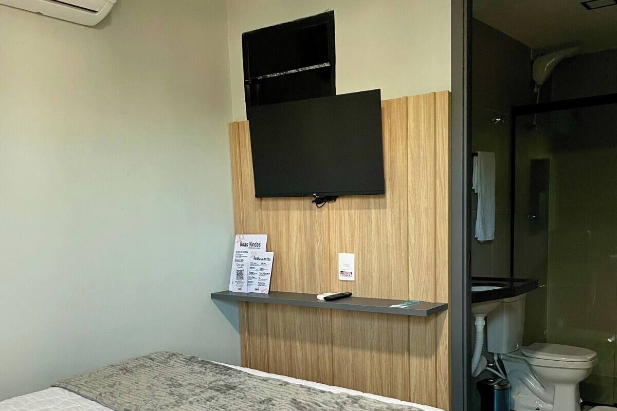 A hotel room with a bed, a mounted television, a small desk with a remote control, and a visible bathroom.