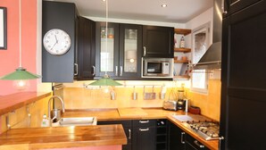 A modern kitchen with dark cabinets, a wooden countertop, a gas stove, a microwave, and a clock on the wall. - House with character, spacious rooms, wooded garden, quiet, free parking (Argelès-sur-Mer)