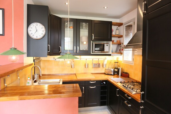 A modern kitchen with dark cabinets, a wooden countertop, a gas stove, a microwave, and a clock on the wall.
