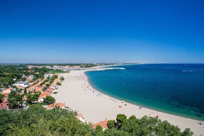 A coastal town with a sandy beach, clear blue sea, and residential buildings with red roofs.