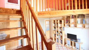 A wooden staircase leading to a loft area with a bookshelf and a television. - House with character, spacious rooms, wooded garden, quiet, free parking (Argelès-sur-Mer)