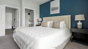 Un dormitorio con una cama grande, dos mesitas de noche con lámparas, un armario y una puerta que da a otra habitación.