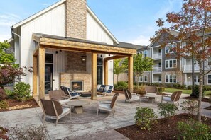 A covered outdoor seating area with a fireplace, surrounded by stone walls and wooden beams, in a residential setting. - Landing | Stunning 2BD, Game Room, Pool (Matthews)