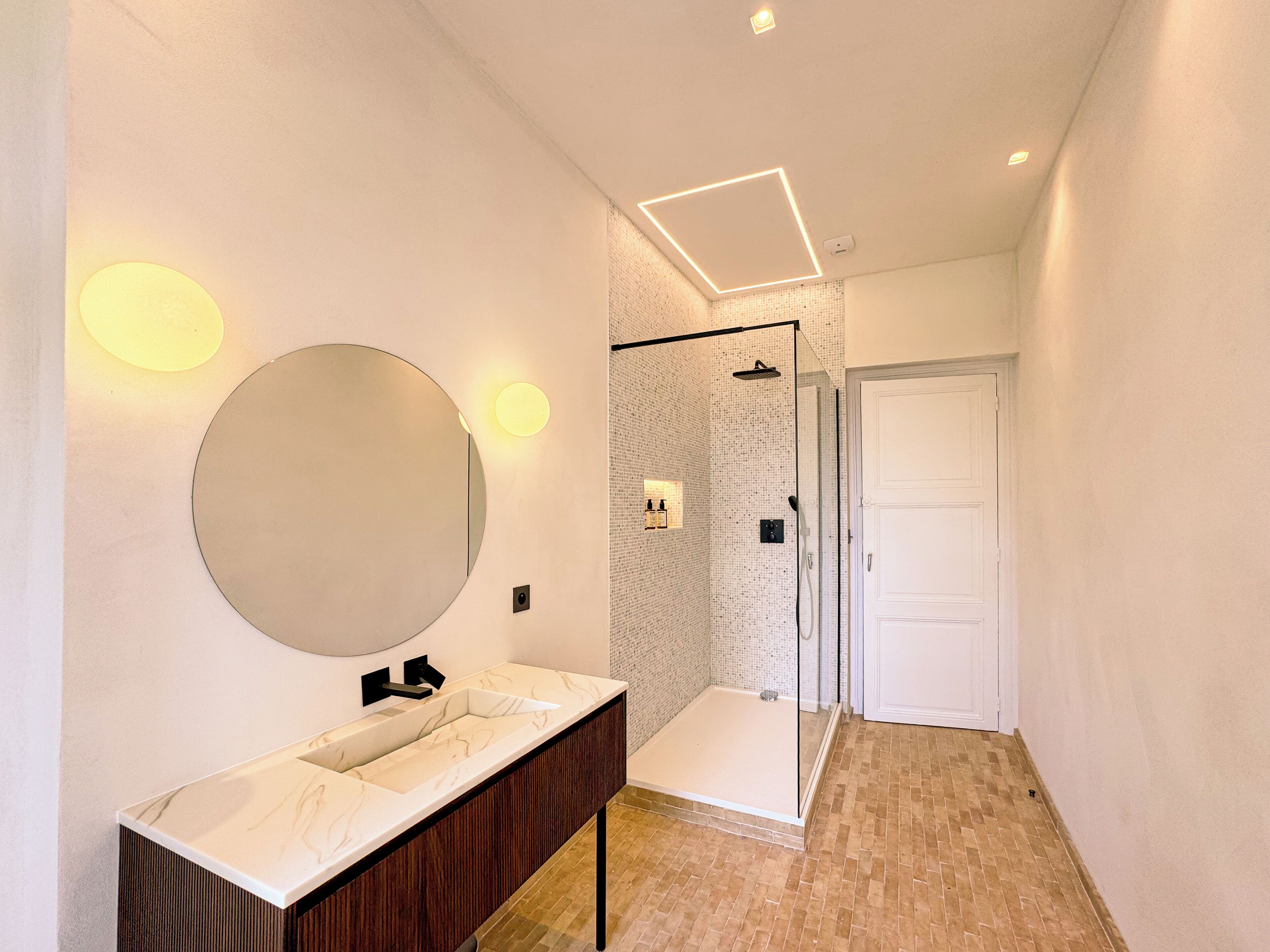 Un bagno moderno con un ampio specchio, un vanità con piano in marmo, una doccia con porta in vetro e un pavimento piastrellato.