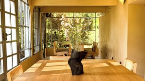 A spacious room with a large wooden table, a black sculpture, and a view of a garden through large windows.