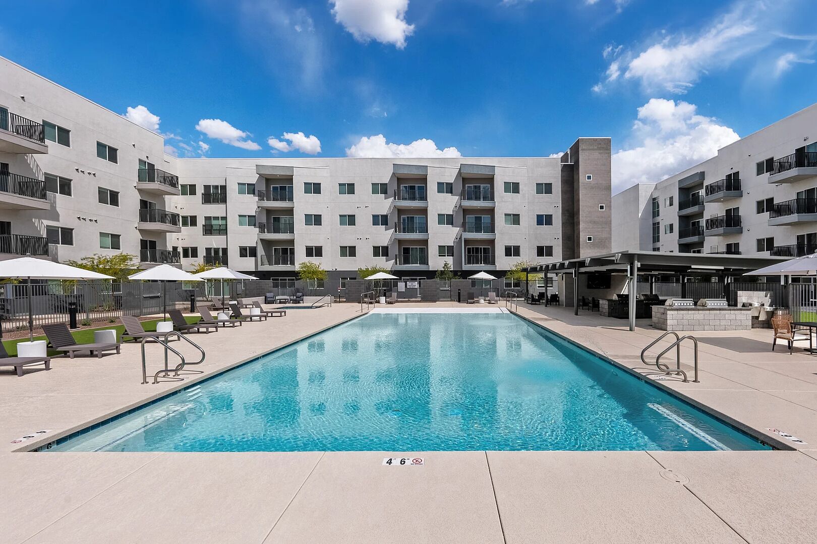 A modern building with a swimming pool, outdoor seating, and a covered patio area.