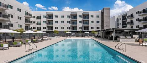 A modern building with a swimming pool, outdoor seating, and a covered patio area.