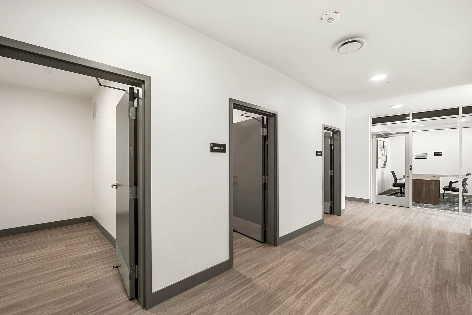 A modern hallway with sliding doors, a fire alarm, and a reception area with a desk and chairs.