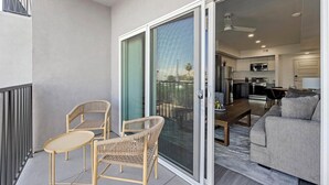 A balcony with wicker chairs and a sofa, a sliding glass door leading to a kitchen and dining area. - Landing | Chic 2BD, Gym, Pool (Phoenix)
