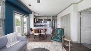 Una sala de estar moderna con un sofá gris, una mesa de comedor redonda con sillas y un sillón verde azulado.