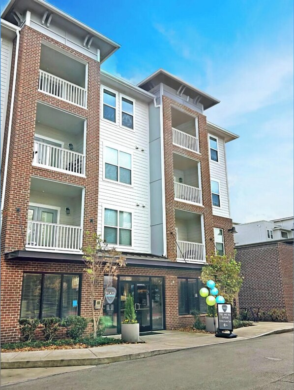 A multi-story apartment building with balconies, a ground-level entrance, and a sign indicating the building is open.