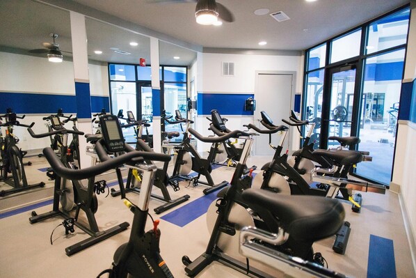 Un gimnasio con varias bicicletas estáticas, espejos y ventanas amplias.