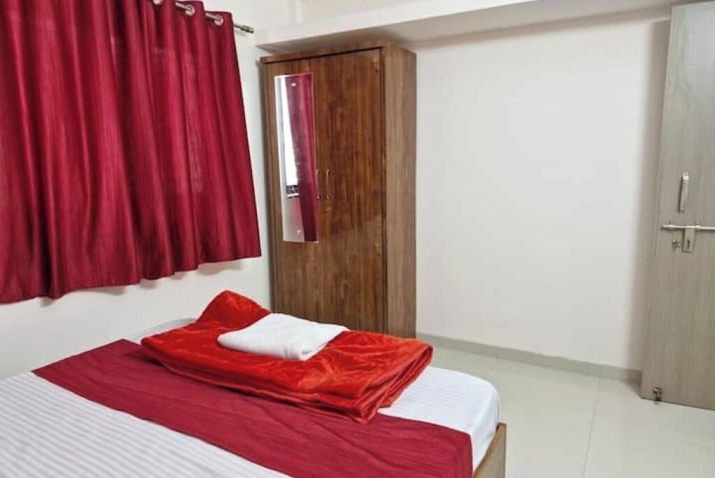 A bedroom with a bed, red curtains, a wooden wardrobe, and a door.