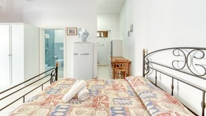 Un dormitorio con cama, escritorio, silla, armario y un baño visible a través de una puerta abierta.