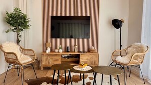 A living room with a TV, two chairs, a small table, a plant, and a lamp.