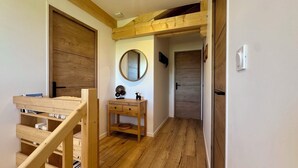 A hallway with wooden flooring, a wooden bench, a small table with drawers, a round mirror, and a door.