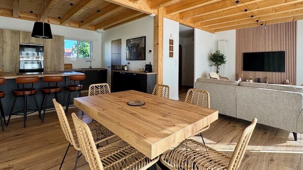 A modern kitchen with a central island, bar stools, and a dining table with chairs.