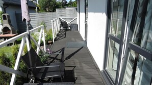 A wooden deck with a chair and a table, a barbecue grill, and a white fence.