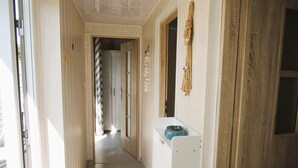 A narrow hallway with a white door at the end, a wooden door on the right, and a white appliance on the left.