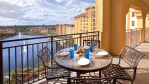 A balcony with a table set for two, overlooking a body of water and cityscape. - Beautiful 1 Bedroom Suite - Orlando, Florida! (Lake Buena Vista)