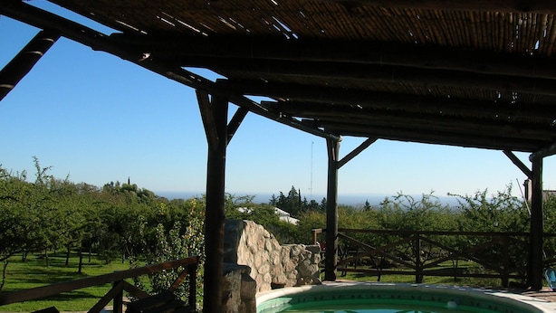 Une piscine extérieure couverte, dotée d’une terrasse en bois et de bancs, entourée d’une végétation luxuriante et offrant une vue dégagée sur l’horizon.