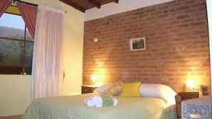 Une chambre avec un mur en briques, un lit avec une literie verte, deux lampes de chevet et une fenêtre avec des rideaux.