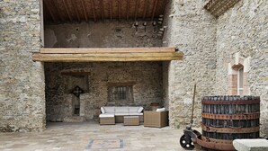 A stone-walled courtyard with a wooden ceiling, stone flooring, a white sofa set, and a large barrel.