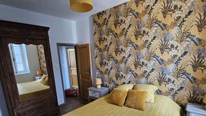 A large bed with a yellow quilt, a wooden wardrobe, a mirror, and a floral wallpaper.