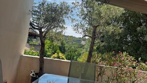 A covered outdoor area with a glass table, a white wall, and a view of trees and hills.